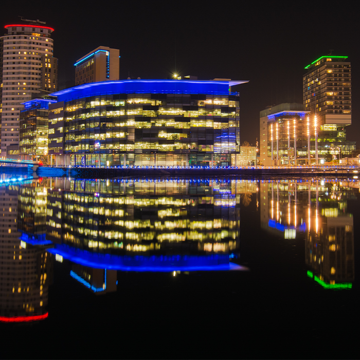 Modern commercial buildings illuminated at night, reflecting in water — typical assets affected by MEES regulations.
